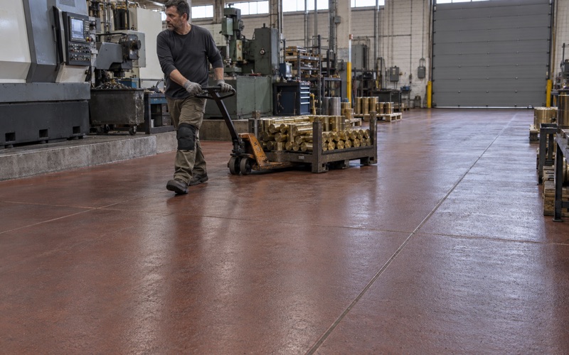 A pallet jack of brass billets pulled across a heavy urethane cement floor in a Cicero metalworking plant.